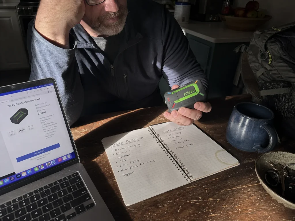 Hiker comparing a ZOLEO satellite communicator against gear notes on a kitchen table