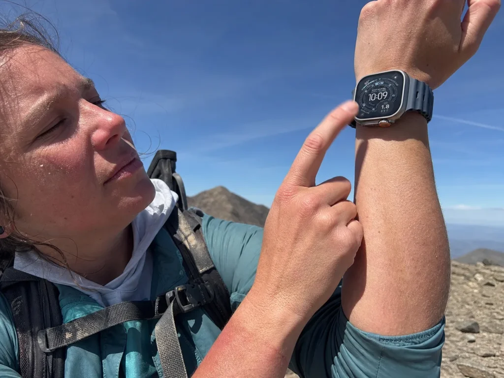 Hiker raising wrist to open sky on an exposed ridge to use satellite SOS on a GPS watch