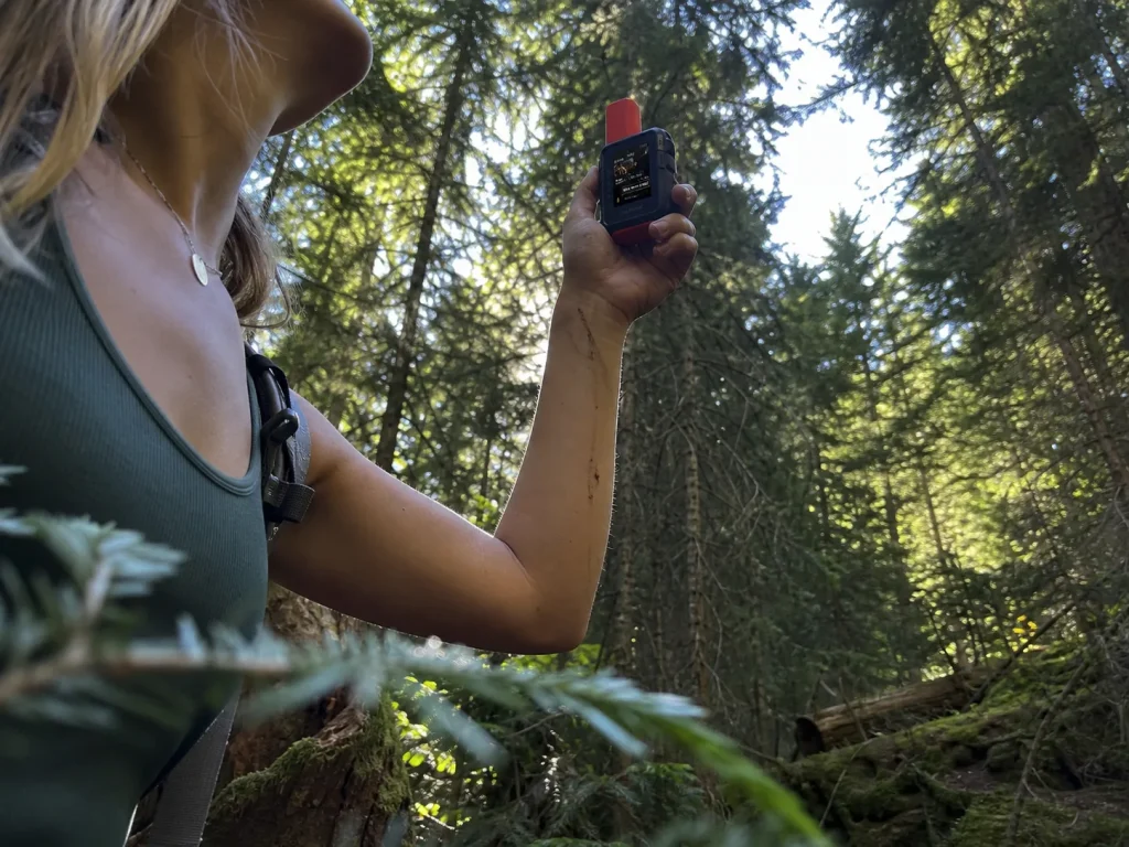Hiker holding a Garmin inReach Mini up toward a gap in dense forest canopy for signal