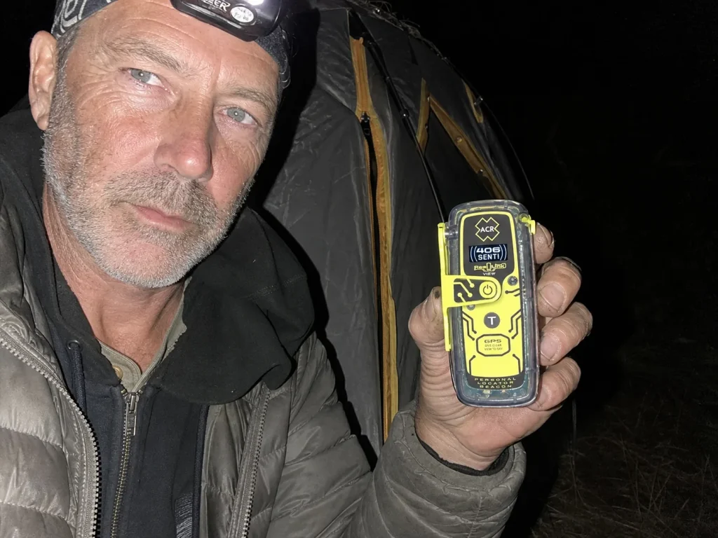 ACR ResQLink View beacon with lit display held at a dusk campsite showing a GPS fix