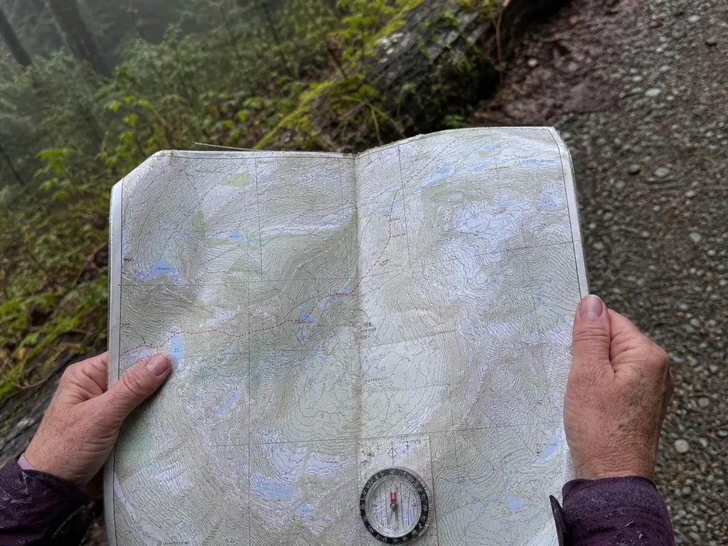 Hiker's hands holding an open National Geographic Trails Illustrated topo map with a compass on top