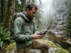 Best Handheld GPS for Hiking Hiker checking a Garmin handheld GPS in dense forest canyon on an overcast morning