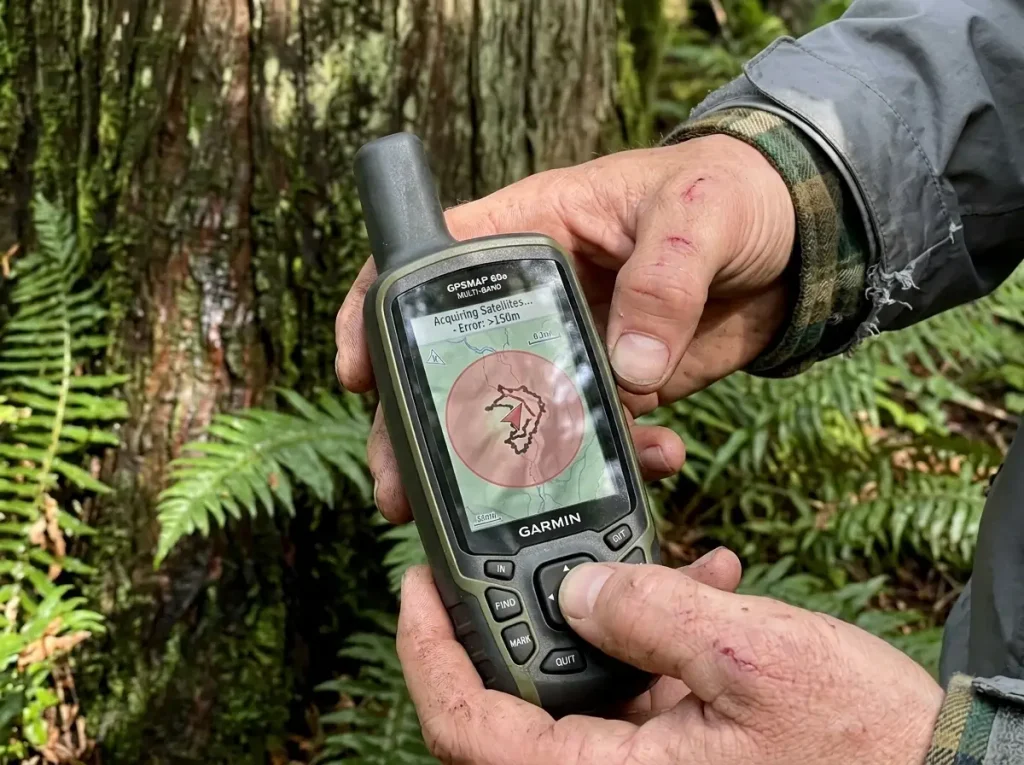 Hands holding a Garmin handheld GPS under dense cedar canopy with a wandering signal