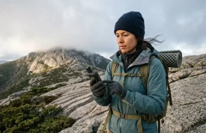 Which Hiking Navigation Devices You Actually Need Hiker checking a handheld GPS on a granite ridge, comparing hiking navigation devices on the trail