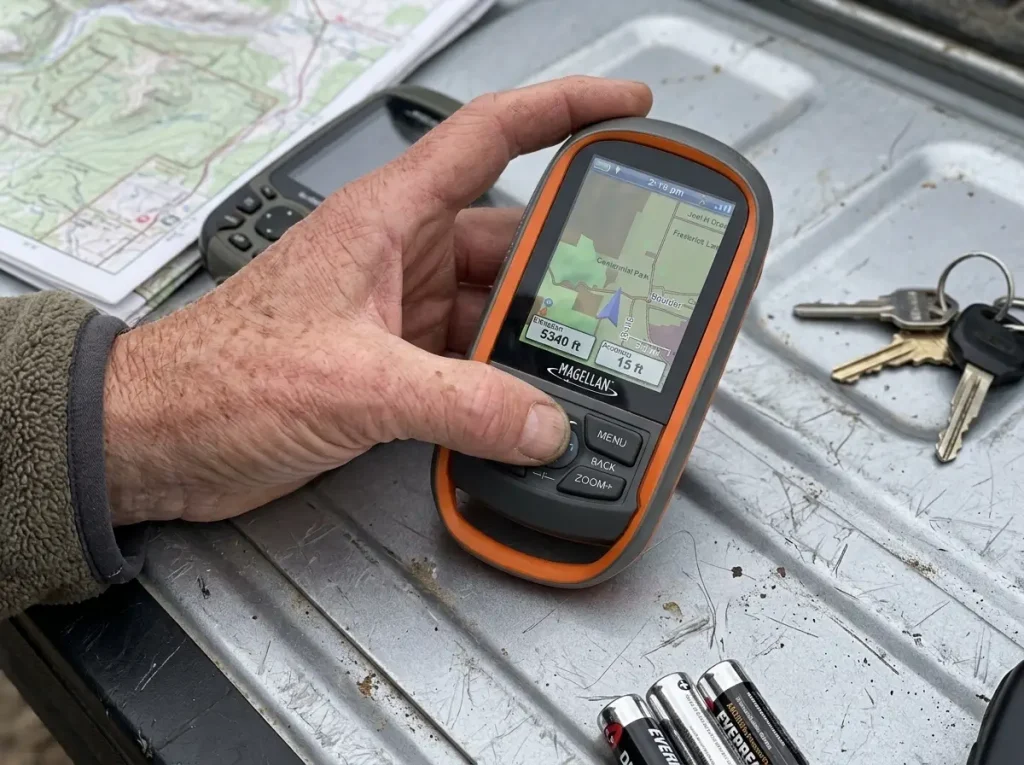 Hands comparing the buttons and screen of a Magellan handheld GPS on a truck tailgate