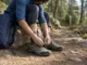 Best Hiking Shoes for Beginners With Untrained Feet Beginner hiker lacing low-cut hiking shoes on a rock at a trailhead