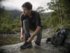 Best Waterproof Hiking Shoes Compared One Clear Winner Man lacing waterproof hiking shoes on a wet rock before crossing a shallow creek at first light