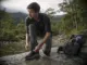Best Waterproof Hiking Shoes Compared One Clear Winner Man lacing waterproof hiking shoes on a wet rock before crossing a shallow creek at first light