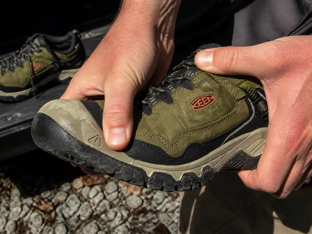 Hands flexing the upper of a waterproof hiking shoe to show the membrane layer under the fabric