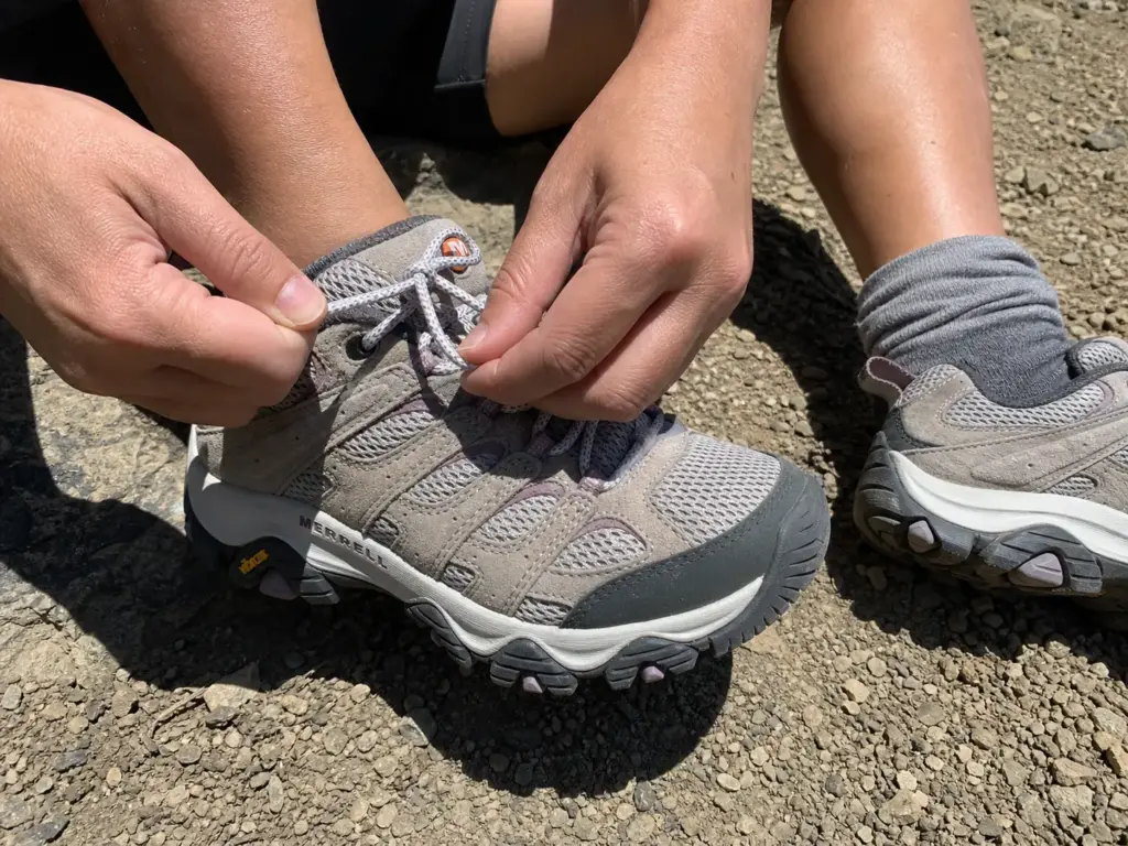 Close-up of a woman relacing a hiking shoe with a heel-lock loop to stop heel slip on descents