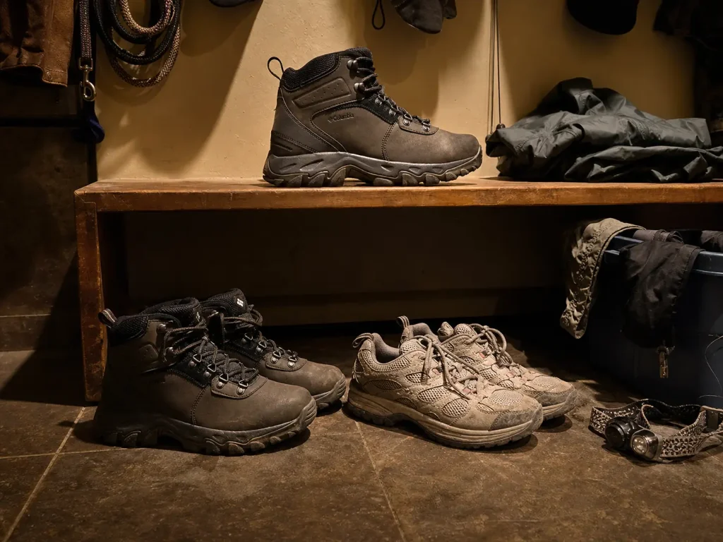 Hiking boots and low-cut hiking shoes on a mudroom floor while choosing a pair for the weekend