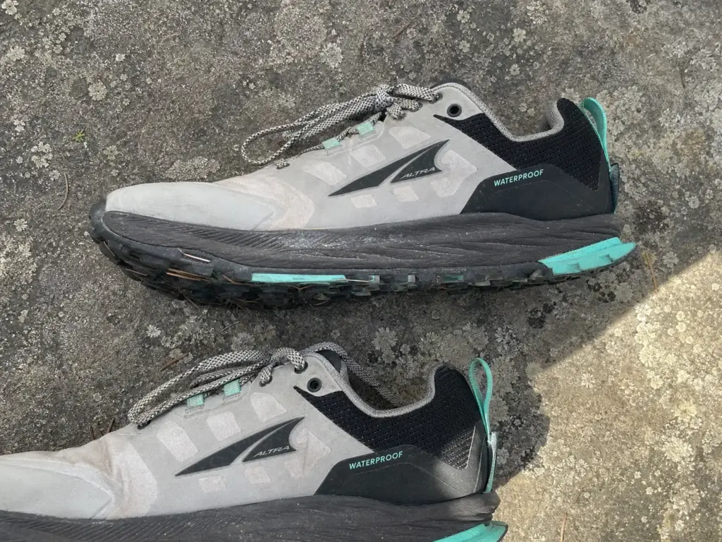 Worn pair of women's hiking shoes on a rock showing a compressed midsole under intact tread