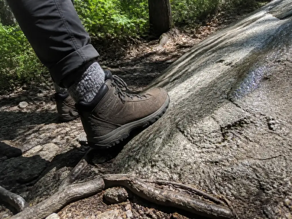 A hiker's mid-cut boot rolling on an uneven rock, the ankle support debate in practice