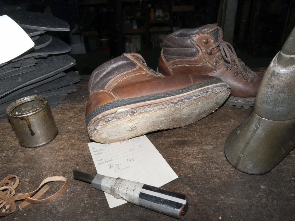 Leather hiking boots on a cobbler's workbench with one outsole stripped for resoling