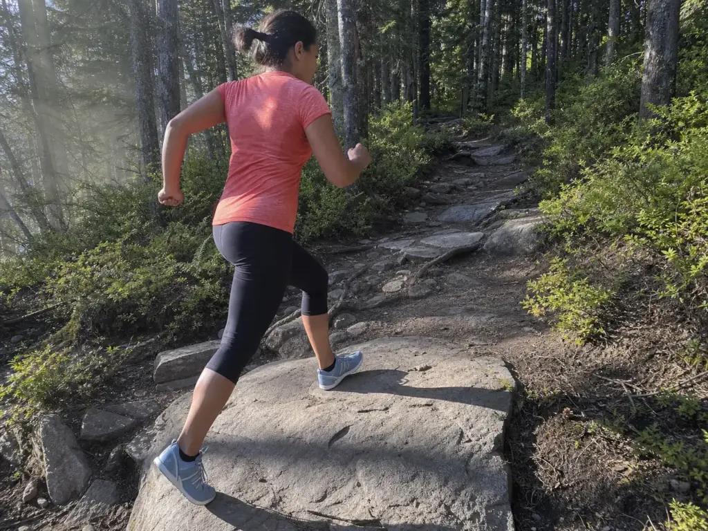 Runner mid-stride on rocky trail landing midfoot in zero-drop shoes, calf visibly loaded