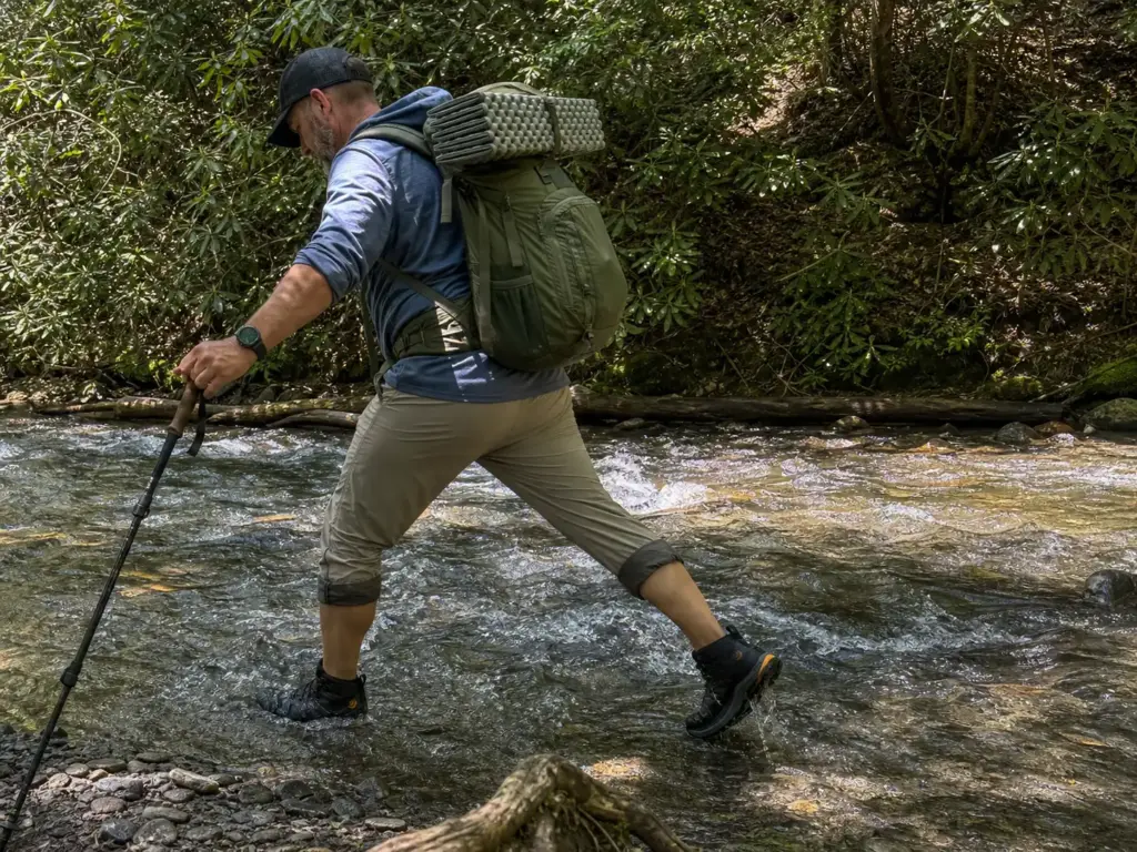 A backpacker crossing a shallow creek in waterproof mid-height trail shoes