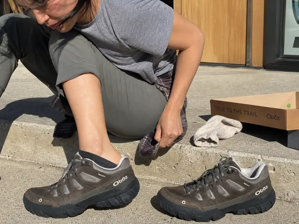 Woman checking heel fit in a hiking shoe next to the men's version of the same model