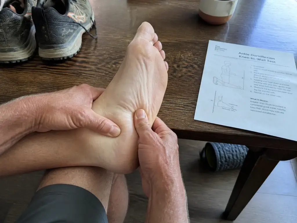 Hands checking ankle flexibility and heel tenderness before switching to zero-drop trail shoes