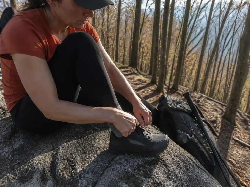 A hiker relacing wide-toebox trail runners at the top of a long descent