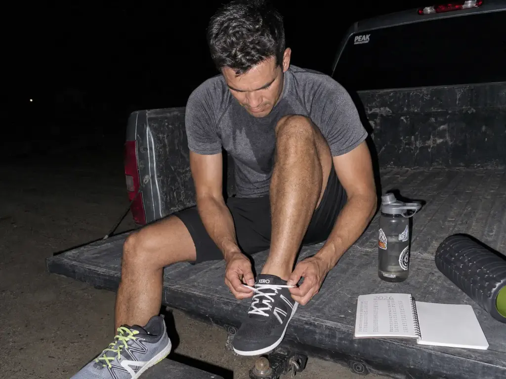 Trail runner swapping into zero-drop shoes at the tailgate while staging a gradual transition