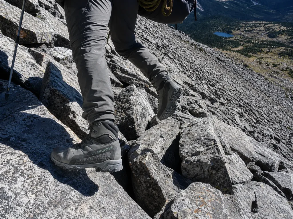 Stiff-soled hiking boots edging across sharp talus blocks on an alpine slope