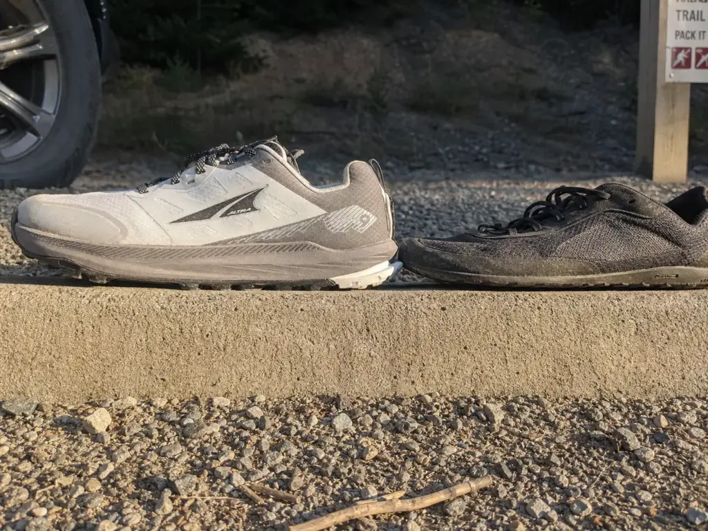 Thick-stacked zero-drop trail shoe beside a thin minimalist one, both with level heel-to-toe platforms