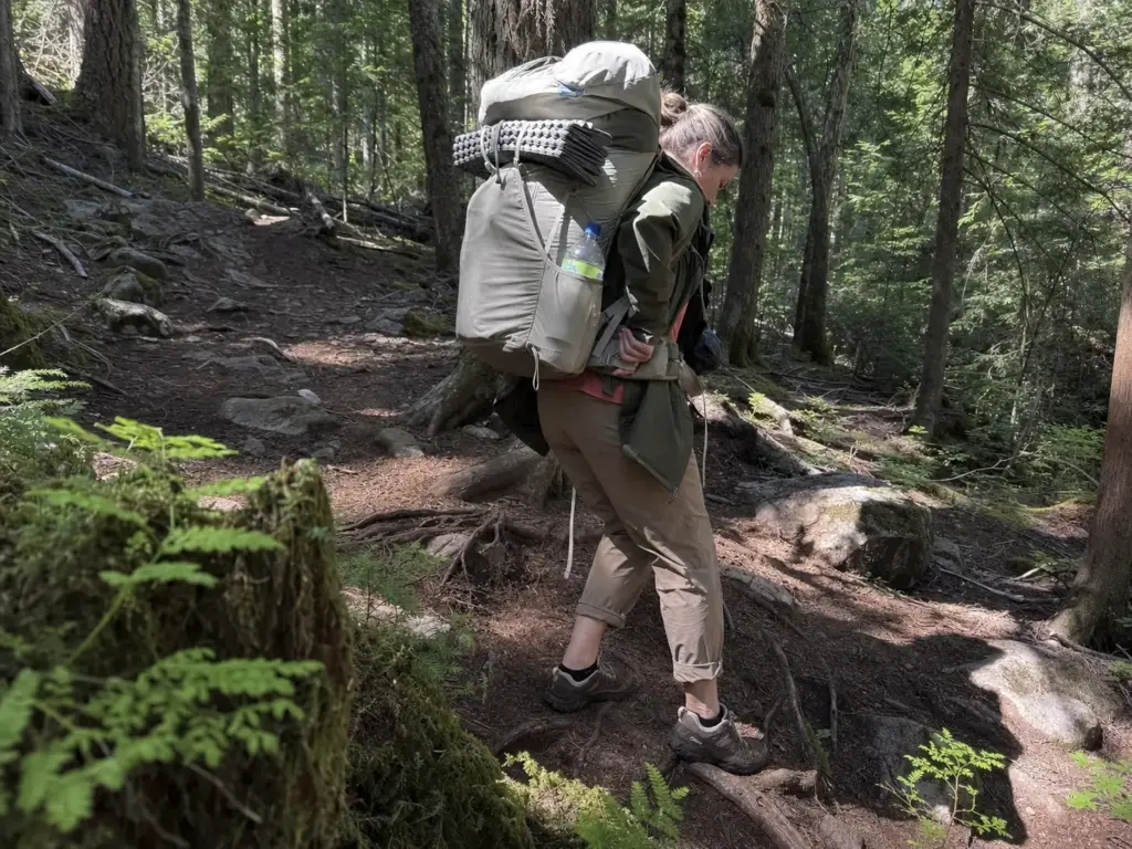Woman in low-cut hiking shoes carrying a loaded multi-day pack down a rooty forest trail
