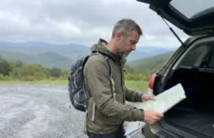 11 Best Hikes in North Carolina Blue Ridge Country Hiker checking a paper map at a Blue Ridge Parkway trailhead in North Carolina on an overcast fall morning