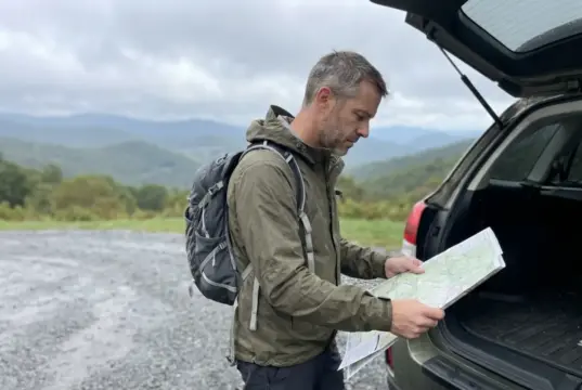 11 Best Hikes in North Carolina Blue Ridge Country Hiker checking a paper map at a Blue Ridge Parkway trailhead in North Carolina on an overcast fall morning