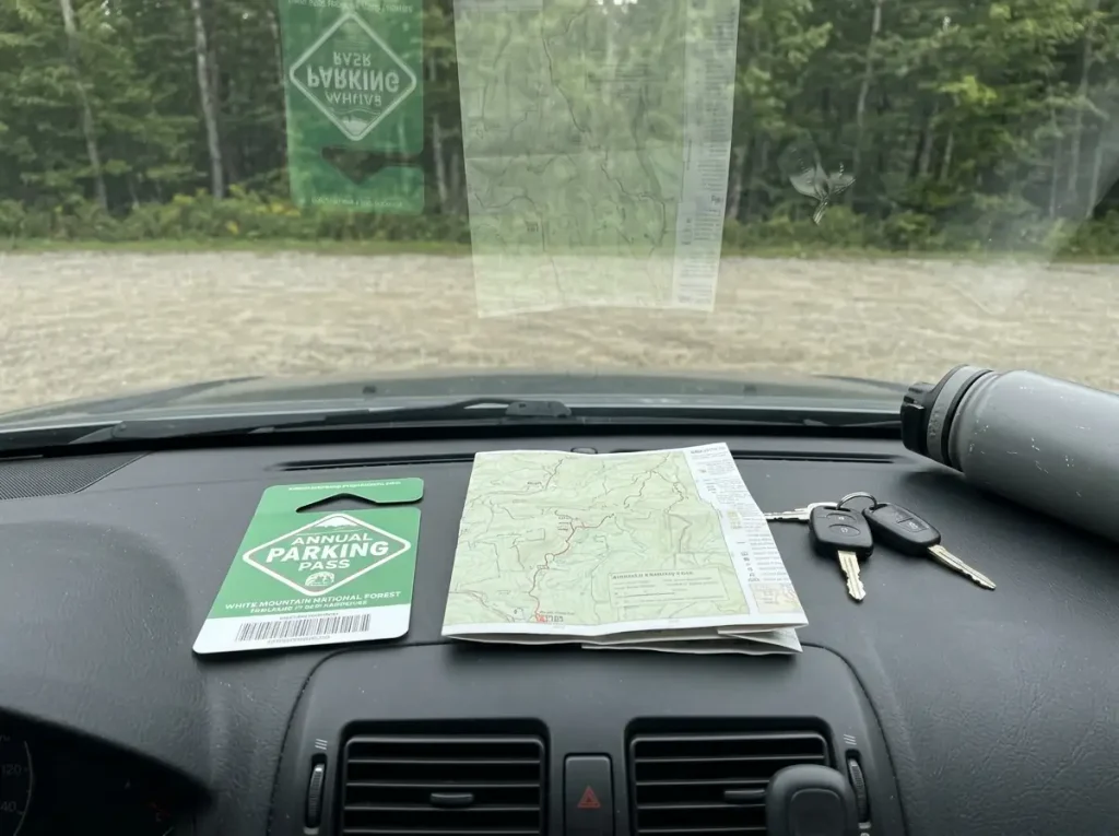 Parking pass and trail map on a car dashboard at a White Mountain National Forest trailhead