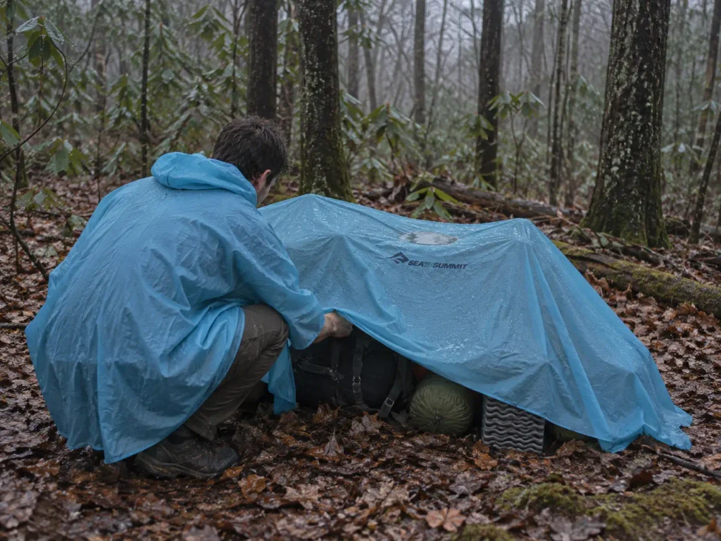 Silnylon poncho pitched as a small tarp over gear at a wet forest campsite