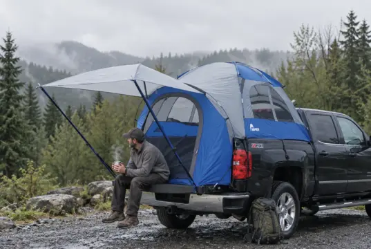 Truck Bed Tent Buying Guide Measure Your Bed First Man sitting on a pickup tailgate with a Napier Sportz truck bed tent pitched over the bed on a cool morning