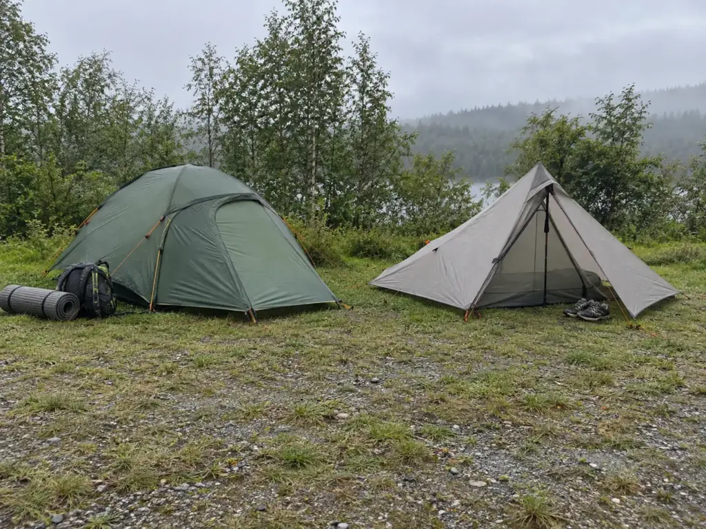 A freestanding dome tent and a trekking-pole shelter pitched side by side at a campsite to compare backpacking tents