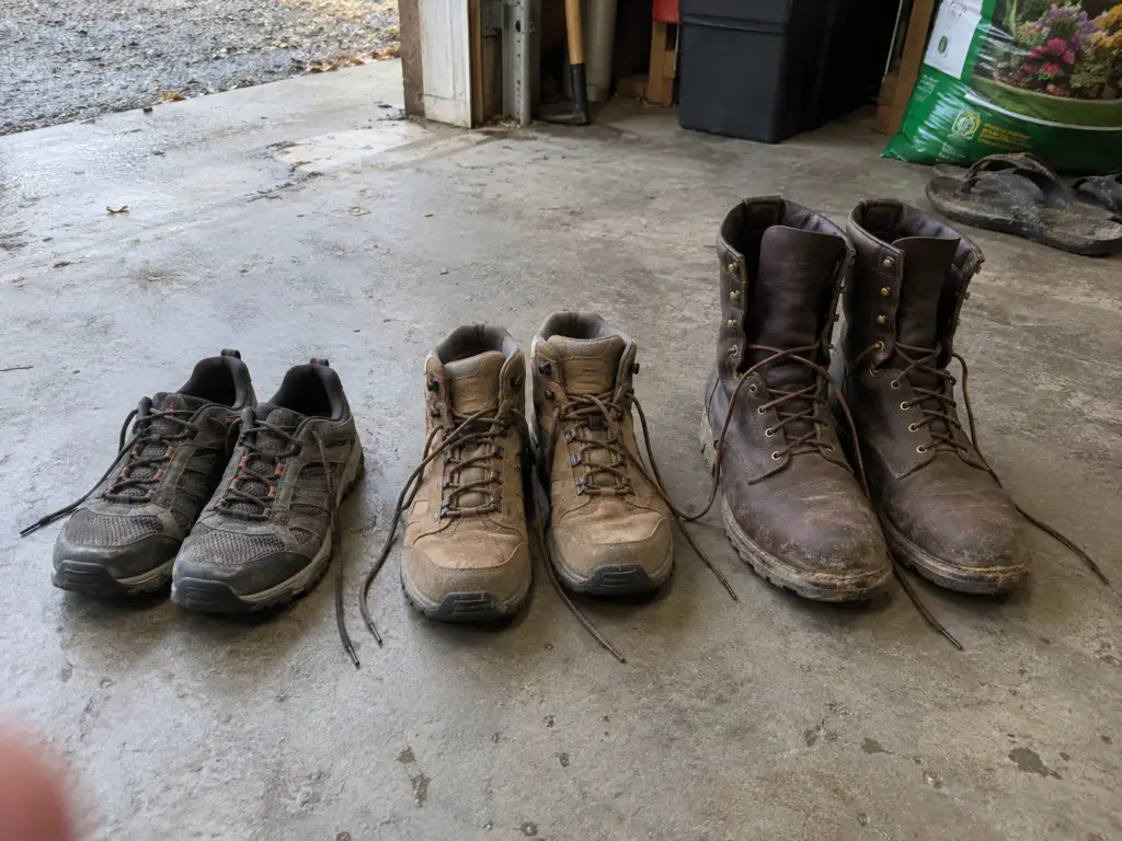 Three pairs of hiking footwear lined up on a garage floor, from a low trail shoe to a tall leather hiking boot