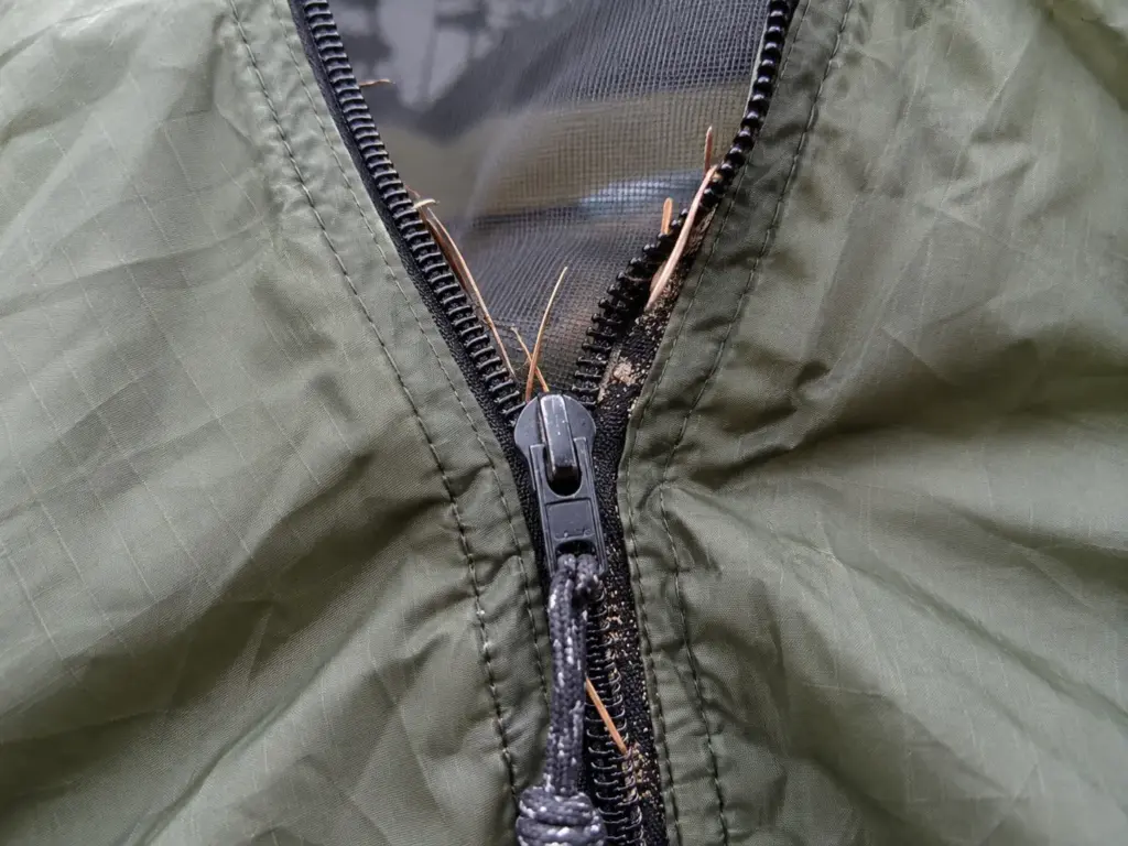 Close-up of a tent door zipper with the teeth gaping open behind the slider and a little grit in the track