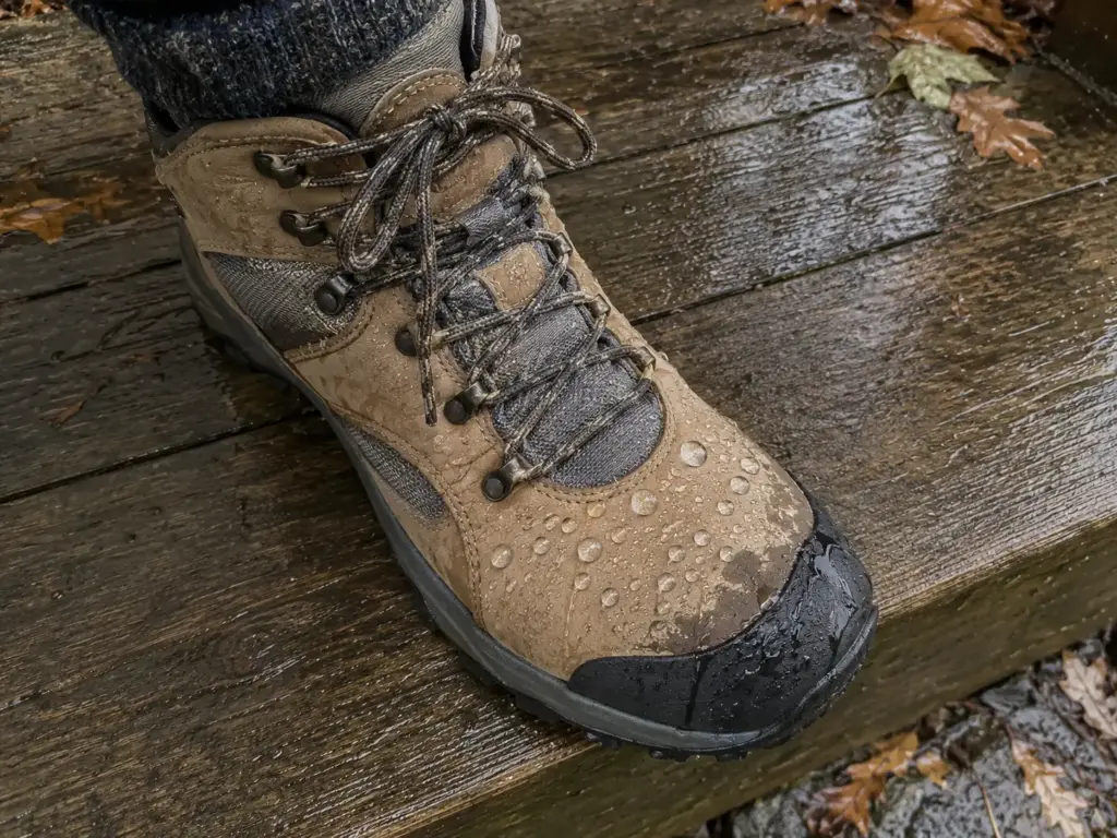 Close view of water beading on the leather toe of a waterproof hiking boot standing on a damp porch step