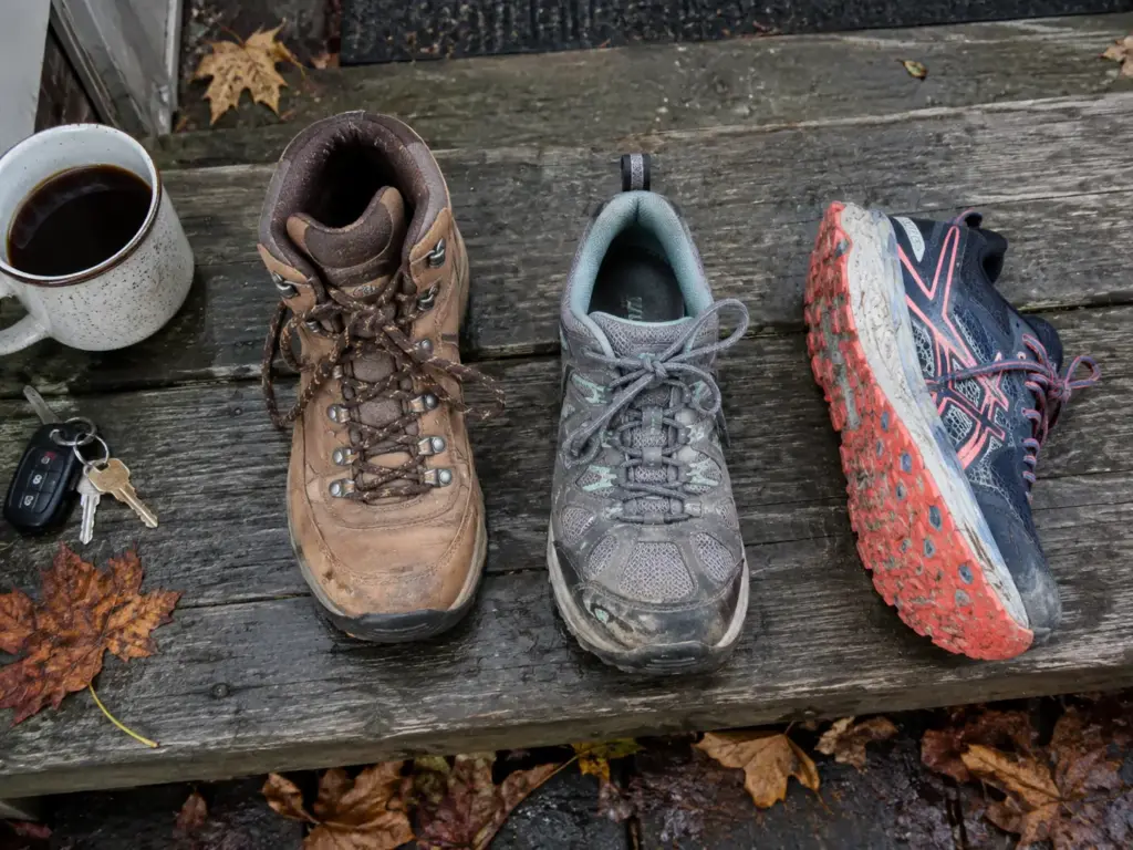 A hiking boot, a low hiking shoe and a trail runner side by side on a porch step to compare women's hiking footwear