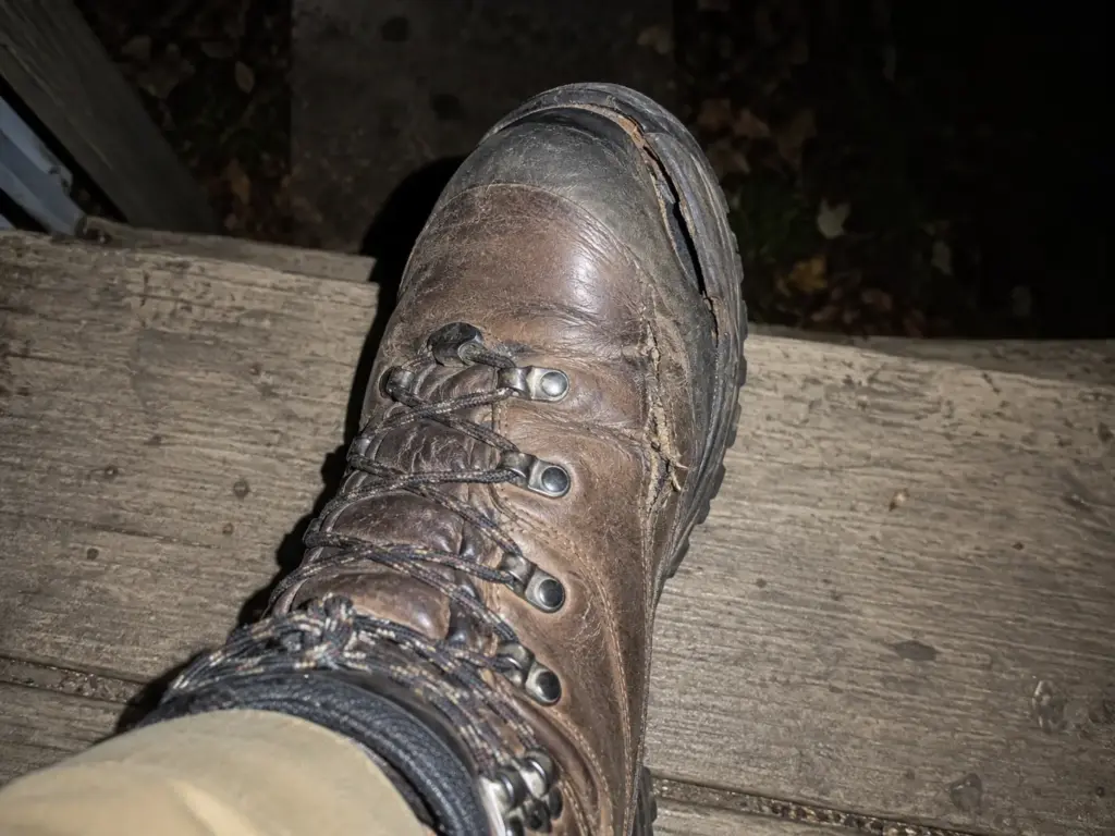 Close photo of a worn leather hiking boot on a porch step showing a frayed seam and a peeling rubber rand
