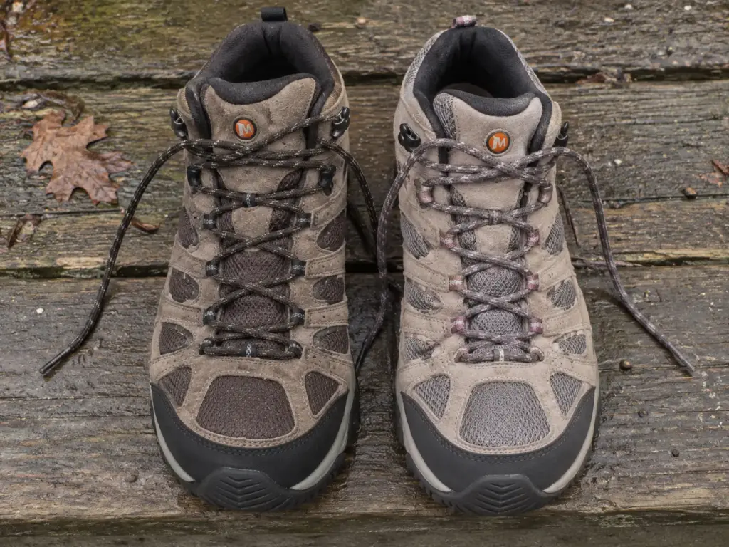 A men's and a women's Merrell Moab 3 Mid Waterproof boot side by side on a porch step showing the width difference