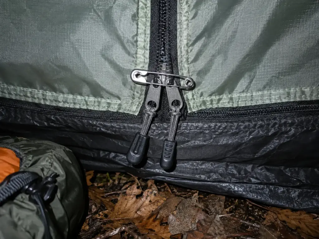 Safety pin holding the two pull tabs of a closed tent door together at night in the light of a phone flash