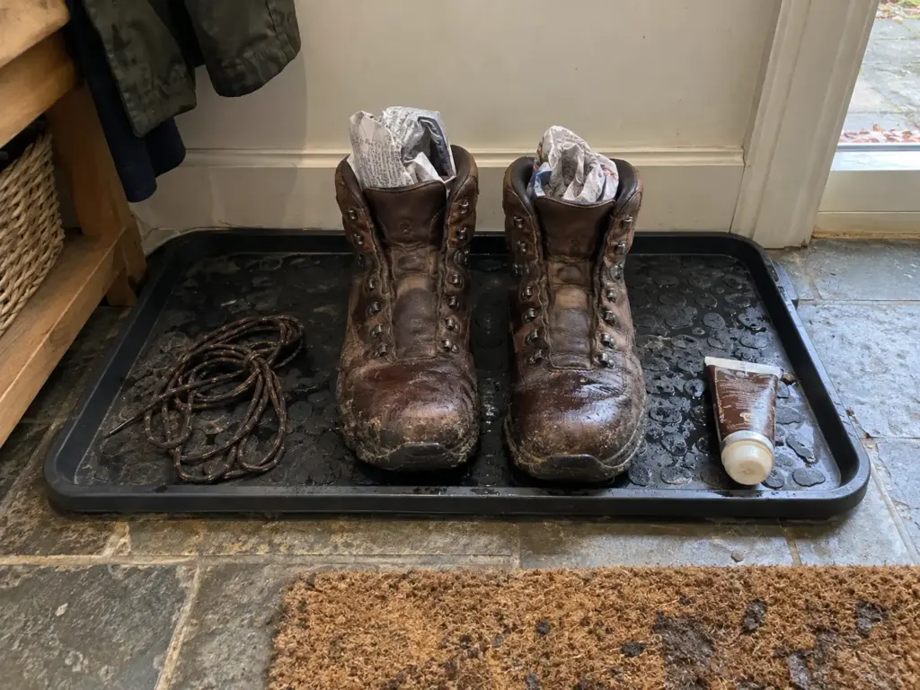 Leather hiking boots stuffed with newspaper drying slowly on a mat by the door, away from any heat source
