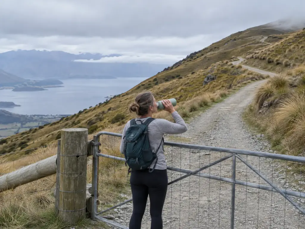 Hiker drinking water at the gate of the Roy's Peak Track above Lake Wānaka in New Zealand