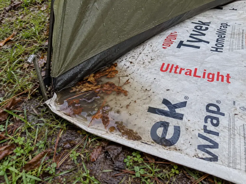 Tyvek groundsheet sticking out past a tent floor with rainwater pooled in it, a common tent moisture mistake