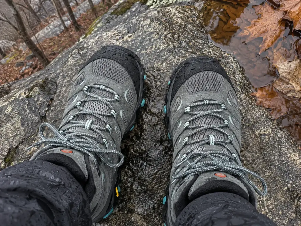 Merrell Moab 3 Mid GTX women's hiking boots on a flat rock beside a trailside puddle after rain