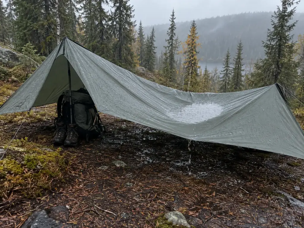 Pitched tarp shelter in light rain with a sagging roof holding a pool of water in the middle of one side