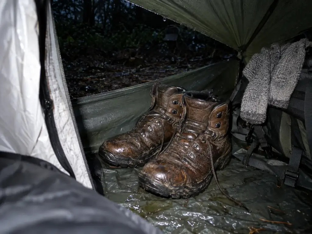 Wet leather hiking boots left overnight in a tent vestibule beside damp wool socks on a rainy multi-day trip