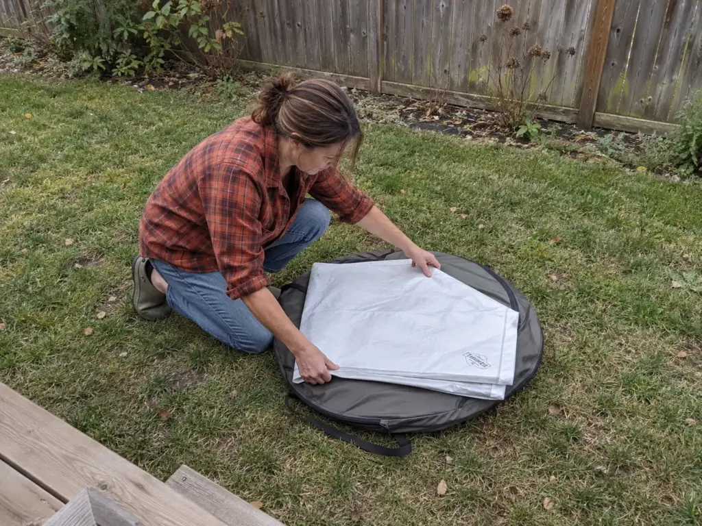 Woman in a backyard laying a white Tyvek ground sheet on a flat round folded pop-out tent on the lawn