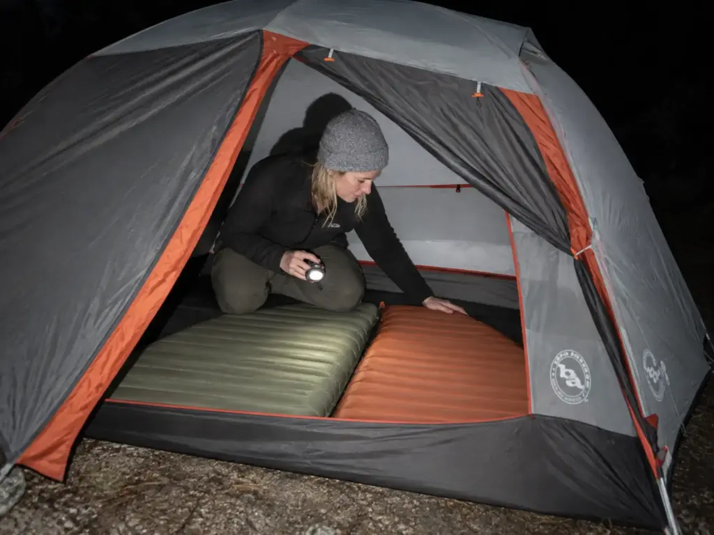 Two sleeping pads lie side by side on the floor of a Big Agnes Copper Spur tent as a woman checks their fit at dusk